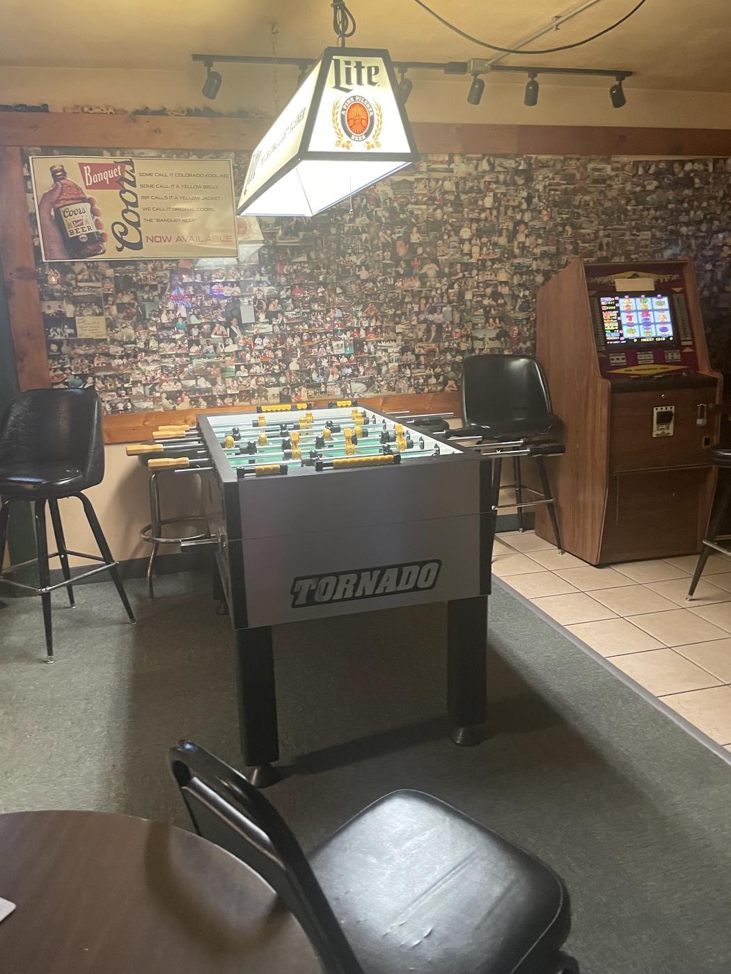 A wall covered floor to ceiling in hundreds of customer photographs, with a foosball table in front of it